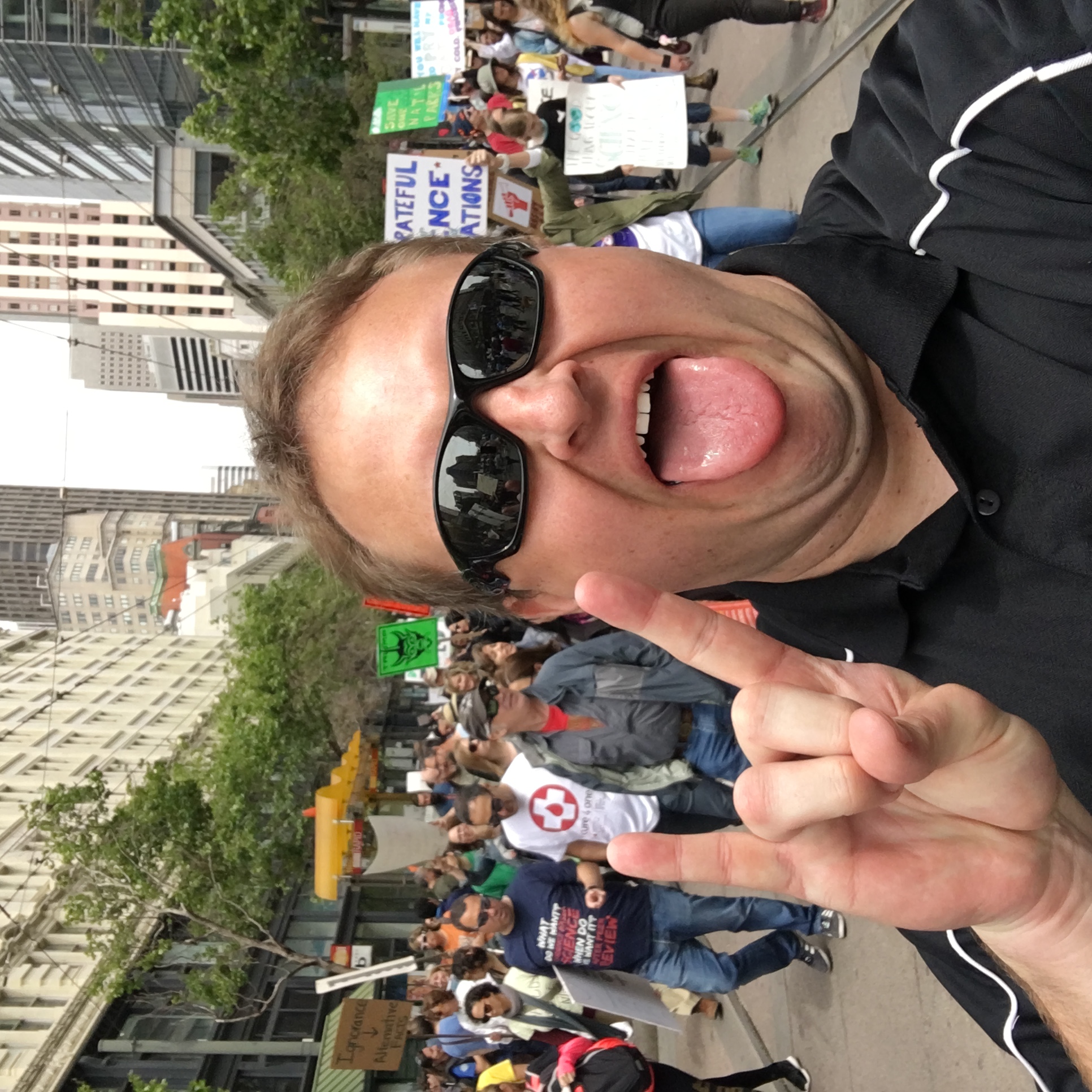 Me at the 2017 Women's March throwing up the horns with marchers behind and in front of me reflected in my sunglasses